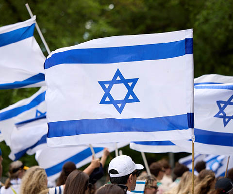 People marching in Israeli Day Parade waving Israeli flags.